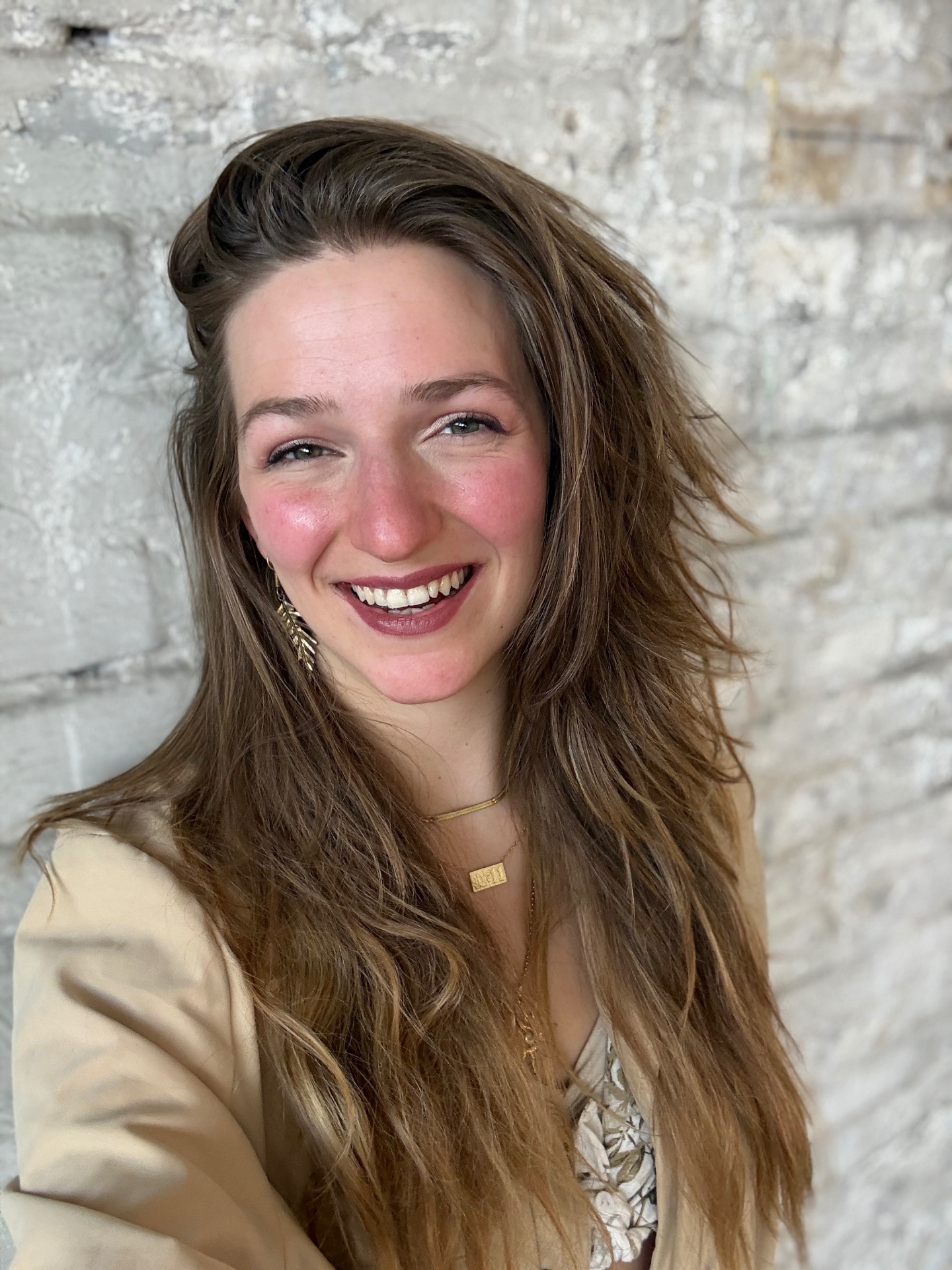 Portrait of Frauke smiling in front of a white brick wall