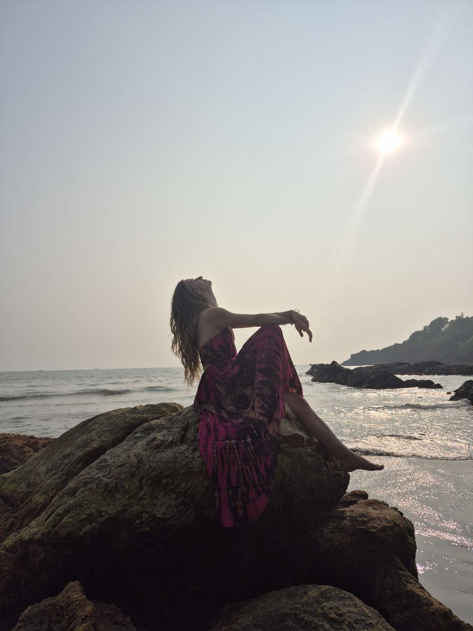 Frauke sitting on a rock by the sea with her face turned towards the sun