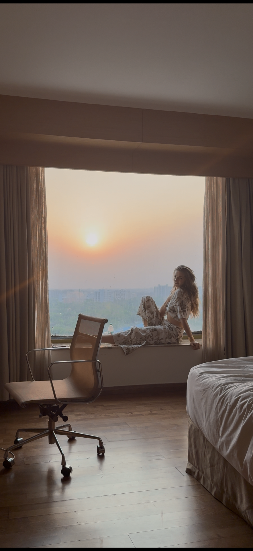 Frauke sitting on a wide windowsill watching the sun rise over a distant city